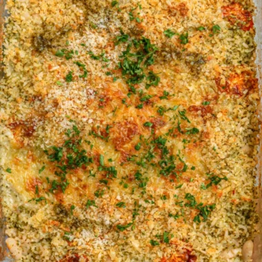 Baked white beans with pesto in a ceramic dish, garnished with fresh herbs.