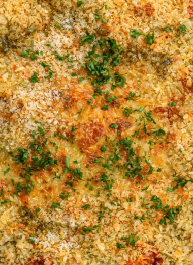 Baked white beans with pesto in a ceramic dish, garnished with fresh herbs.
